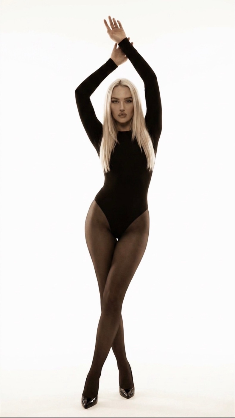 Grace standing with her arms raised in a black bodysuit